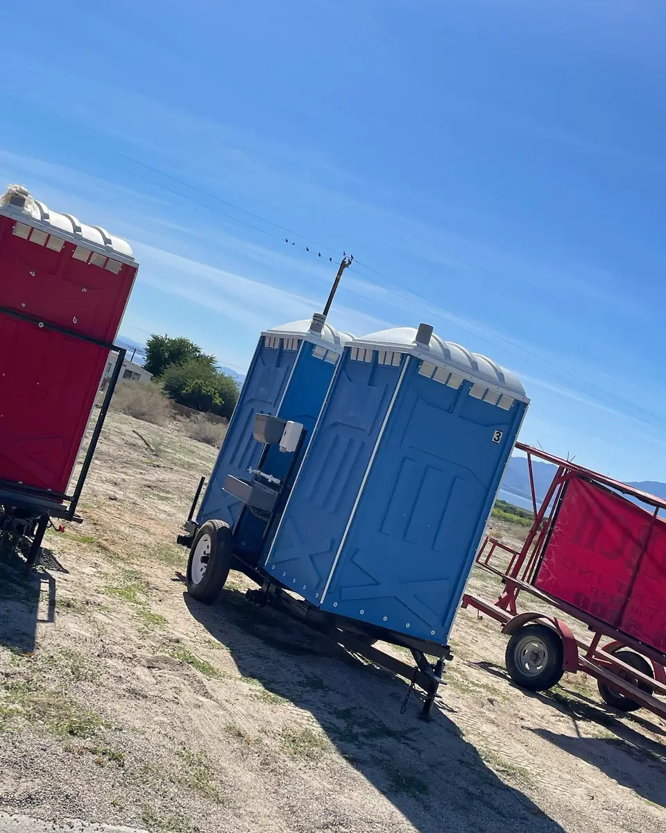 Blue porta potty on a towable trailer in a field